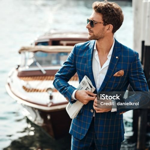 Young handsome man in classic suit over the blurred lake buttoning his jacket